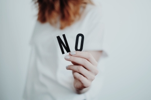 Woman in white shirt and red hair holding up the letters ‘N’ and ‘O’ with a white background.